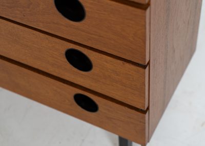 Teak shoe cabinet (Germany, 1960s). The cabinet features two small drawers and three shelves for shoe storage. It is made of teak and has a black lacquered frame with black inset handles that allow for proper ventilation. The cabinet is in good condition, with some visible signs of use.