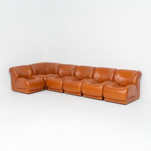 Modular sofa by Doimo Salotti (Italy, 1970s). Striking and bold modular seating system consisting of five identical elements and one corner piece, upholstered in their original cognac leather. Can be arranged as a sofa or used as individual lounge chairs. Low, sculptural design with generous padding, offering both strong visual impact and excellent comfort. The sofa is in very good condition with some age-related signs of use, as shown in the pictures. Most traces of use are discreet and not immediately visible. Marked by the maker.