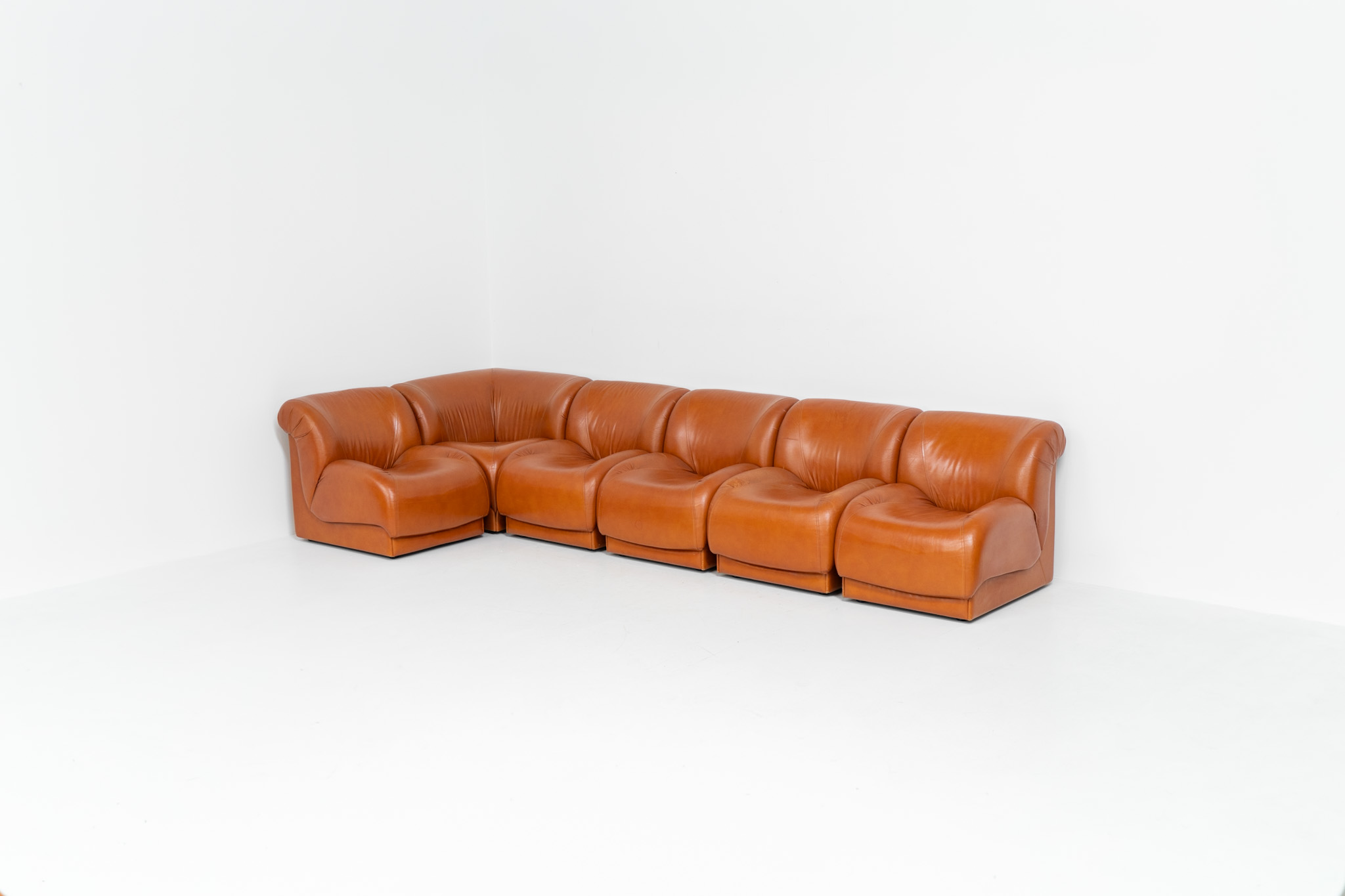 Modular sofa by Doimo Salotti (Italy, 1970s). Striking and bold modular seating system consisting of five identical elements and one corner piece, upholstered in their original cognac leather. Can be arranged as a sofa or used as individual lounge chairs. Low, sculptural design with generous padding, offering both strong visual impact and excellent comfort. The sofa is in very good condition with some age-related signs of use, as shown in the pictures. Most traces of use are discreet and not immediately visible. Marked by the maker.
