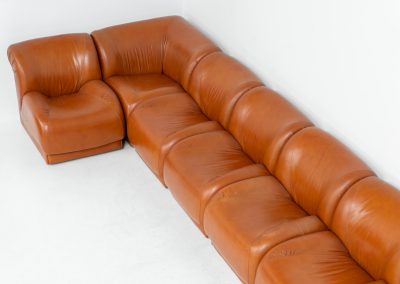 Modular sofa by Doimo Salotti (Italy, 1970s). Striking and bold modular seating system consisting of five identical elements and one corner piece, upholstered in their original cognac leather. Can be arranged as a sofa or used as individual lounge chairs. Low, sculptural design with generous padding, offering both strong visual impact and excellent comfort. The sofa is in very good condition with some age-related signs of use, as shown in the pictures. Most traces of use are discreet and not immediately visible. Marked by the maker.