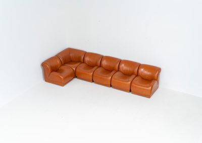 Modular sofa by Doimo Salotti (Italy, 1970s). Striking and bold modular seating system consisting of five identical elements and one corner piece, upholstered in their original cognac leather. Can be arranged as a sofa or used as individual lounge chairs. Low, sculptural design with generous padding, offering both strong visual impact and excellent comfort. The sofa is in very good condition with some age-related signs of use, as shown in the pictures. Most traces of use are discreet and not immediately visible. Marked by the maker.