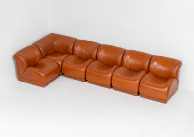 Modular sofa by Doimo Salotti (Italy, 1970s). Striking and bold modular seating system consisting of five identical elements and one corner piece, upholstered in their original cognac leather. Can be arranged as a sofa or used as individual lounge chairs. Low, sculptural design with generous padding, offering both strong visual impact and excellent comfort. The sofa is in very good condition with some age-related signs of use, as shown in the pictures. Most traces of use are discreet and not immediately visible. Marked by the maker.