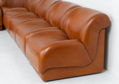 Modular sofa by Doimo Salotti (Italy, 1970s). Striking and bold modular seating system consisting of five identical elements and one corner piece, upholstered in their original cognac leather. Can be arranged as a sofa or used as individual lounge chairs. Low, sculptural design with generous padding, offering both strong visual impact and excellent comfort. The sofa is in very good condition with some age-related signs of use, as shown in the pictures. Most traces of use are discreet and not immediately visible. Marked by the maker.
