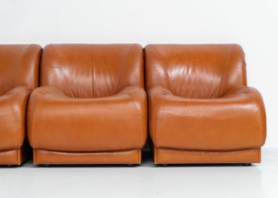 Modular sofa by Doimo Salotti (Italy, 1970s). Striking and bold modular seating system consisting of five identical elements and one corner piece, upholstered in their original cognac leather. Can be arranged as a sofa or used as individual lounge chairs. Low, sculptural design with generous padding, offering both strong visual impact and excellent comfort. The sofa is in very good condition with some age-related signs of use, as shown in the pictures. Most traces of use are discreet and not immediately visible. Marked by the maker.