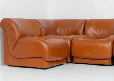 Modular sofa by Doimo Salotti (Italy, 1970s). Striking and bold modular seating system consisting of five identical elements and one corner piece, upholstered in their original cognac leather. Can be arranged as a sofa or used as individual lounge chairs. Low, sculptural design with generous padding, offering both strong visual impact and excellent comfort. The sofa is in very good condition with some age-related signs of use, as shown in the pictures. Most traces of use are discreet and not immediately visible. Marked by the maker.