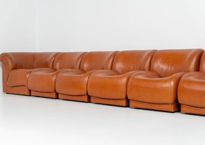 Modular sofa by Doimo Salotti (Italy, 1970s). Striking and bold modular seating system consisting of five identical elements and one corner piece, upholstered in their original cognac leather. Can be arranged as a sofa or used as individual lounge chairs. Low, sculptural design with generous padding, offering both strong visual impact and excellent comfort. The sofa is in very good condition with some age-related signs of use, as shown in the pictures. Most traces of use are discreet and not immediately visible. Marked by the maker.