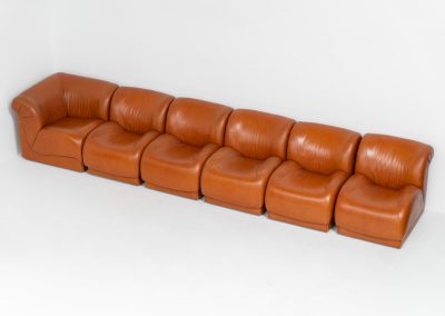 Modular sofa by Doimo Salotti (Italy, 1970s). Striking and bold modular seating system consisting of five identical elements and one corner piece, upholstered in their original cognac leather. Can be arranged as a sofa or used as individual lounge chairs. Low, sculptural design with generous padding, offering both strong visual impact and excellent comfort. The sofa is in very good condition with some age-related signs of use, as shown in the pictures. Most traces of use are discreet and not immediately visible. Marked by the maker.