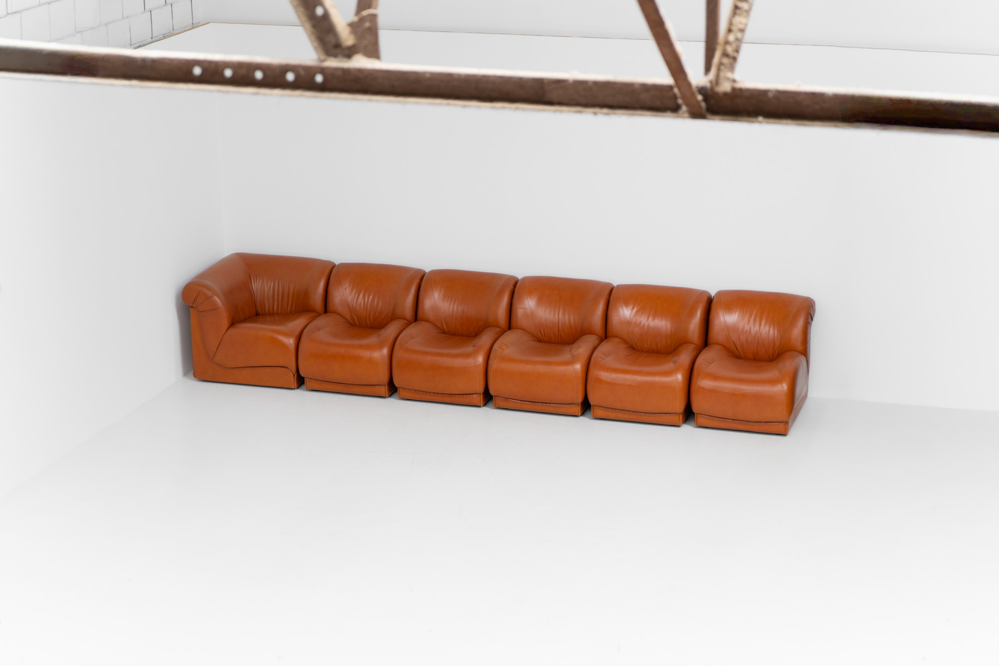 Modular sofa by Doimo Salotti (Italy, 1970s). Striking and bold modular seating system consisting of five identical elements and one corner piece, upholstered in their original cognac leather. Can be arranged as a sofa or used as individual lounge chairs. Low, sculptural design with generous padding, offering both strong visual impact and excellent comfort. The sofa is in very good condition with some age-related signs of use, as shown in the pictures. Most traces of use are discreet and not immediately visible. Marked by the maker.