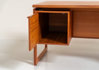 Teak executive writing desk by G.V. Møbler (Denmark, 1960s). This exceptionally beautiful piece is a true example of top-quality Danish craftsmanship. Made from teak, it showcases elegant aesthetics with softly rounded edges and a floating desk top. It offers three very deep drawers, a cabinet, a solid teak top, a stunning sled base and a finished backside, making it an ideal piece for placement in the center of a room. The desk is in excellent condition.