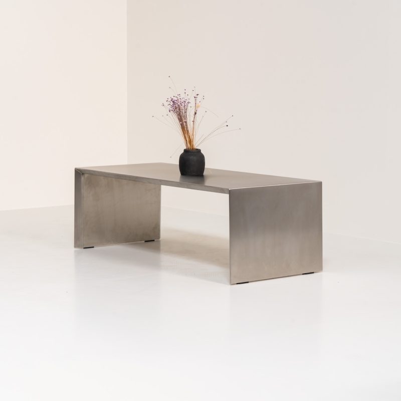 Brushed stainless steel coffee table (The Netherlands, 1980s). A striking coffee table that effortlessly balances weight and lightness. It features a minimalist aesthetic defined by clean, architectural lines, seamlessly pleated corners, and subtly beveled edges. The table is in good vintage condition with some age related wear and scratches.