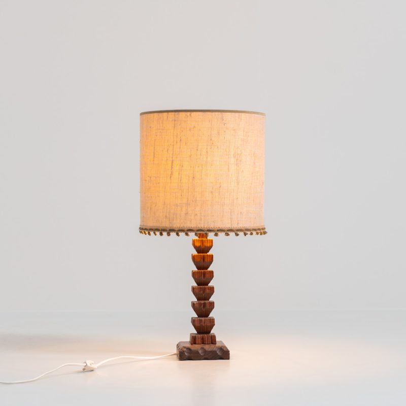 Sculptural table lamp in the manner of Charles Dudouyt (France, 1950s). This lamp offers a refined blend of beautiful textures and a highly sculptural silhouette. It has a handcrafted wooden base with lots of detail, complimented by a linnen shade. The lamp remains in splendid condition.