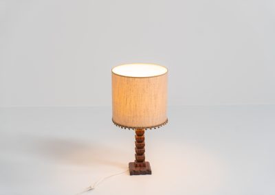 Sculptural table lamp in the manner of Charles Dudouyt (France, 1950s). This lamp offers a refined blend of beautiful textures and a highly sculptural silhouette. It has a handcrafted wooden base with lots of detail, complimented by a linnen shade. The lamp remains in splendid condition.