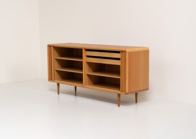 Oak sideboard with tambour doors by Kibaek Møbelfabrik (Denmark, 1960s). A beautifully crafted piece showcasing exceptional Danish design and craftsmanship. It features two tambour doors with adjustable shelves and two drawers on the inside, offering generous and flexible storage. The softly rounded edges and organic lines give the sideboard a refined, timeless character. In good condition with a mark/stain on top.