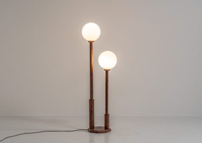 Wood & opal glass floor lamp, 1970s. Vintage floor lamp featuring a sculptural, geometric wooden base with two slender stems at different heights, each topped with a spherical opaline glass shade. The warm-toned wood and softly diffused light create a beautiful balance between architectural form and understated elegance. A distinctive vintage piece that works as both a functional light source and a sculptural accent in a contemporary or mid-century inspired interior. The lamp is in very good vintage condition overall, with a subtle historic repair to the wood near the base of one glass support.