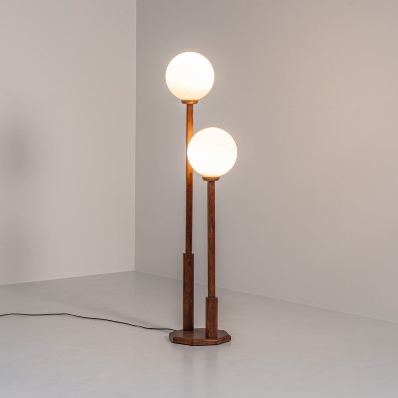 Wood & opal glass floor lamp, 1970s. Vintage floor lamp featuring a sculptural, geometric wooden base with two slender stems at different heights, each topped with a spherical opaline glass shade. The warm-toned wood and softly diffused light create a beautiful balance between architectural form and understated elegance. A distinctive vintage piece that works as both a functional light source and a sculptural accent in a contemporary or mid-century inspired interior. The lamp is in very good vintage condition overall, with a subtle historic repair to the wood near the base of one glass support.