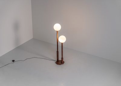 Wood & opal glass floor lamp, 1970s. Vintage floor lamp featuring a sculptural, geometric wooden base with two slender stems at different heights, each topped with a spherical opaline glass shade. The warm-toned wood and softly diffused light create a beautiful balance between architectural form and understated elegance. A distinctive vintage piece that works as both a functional light source and a sculptural accent in a contemporary or mid-century inspired interior. The lamp is in very good vintage condition overall, with a subtle historic repair to the wood near the base of one glass support.