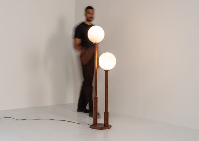 Wood & opal glass floor lamp, 1970s. Vintage floor lamp featuring a sculptural, geometric wooden base with two slender stems at different heights, each topped with a spherical opaline glass shade. The warm-toned wood and softly diffused light create a beautiful balance between architectural form and understated elegance. A distinctive vintage piece that works as both a functional light source and a sculptural accent in a contemporary or mid-century inspired interior. The lamp is in very good vintage condition overall, with a subtle historic repair to the wood near the base of one glass support.